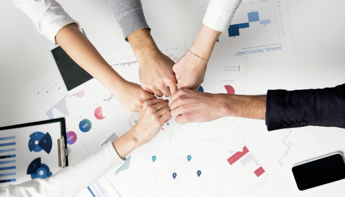 Free Colleagues celebrate success with a fist bump over financial charts depicting teamwork and unity. Stock Photo